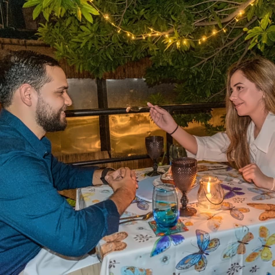 Una pareja comparte una cena a la luz de las velas en el jardín de Musa, bajo una guirnalda de luces.