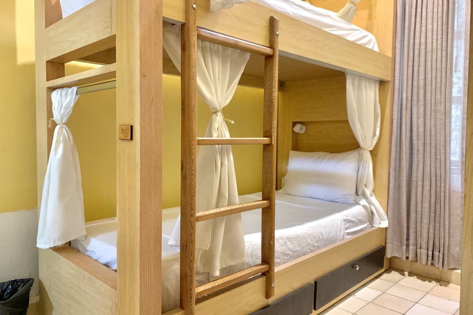 Dormitorio de 4 camas: literas de madera con cortinas blancas, escalera y cajones bajo la cama inferior.