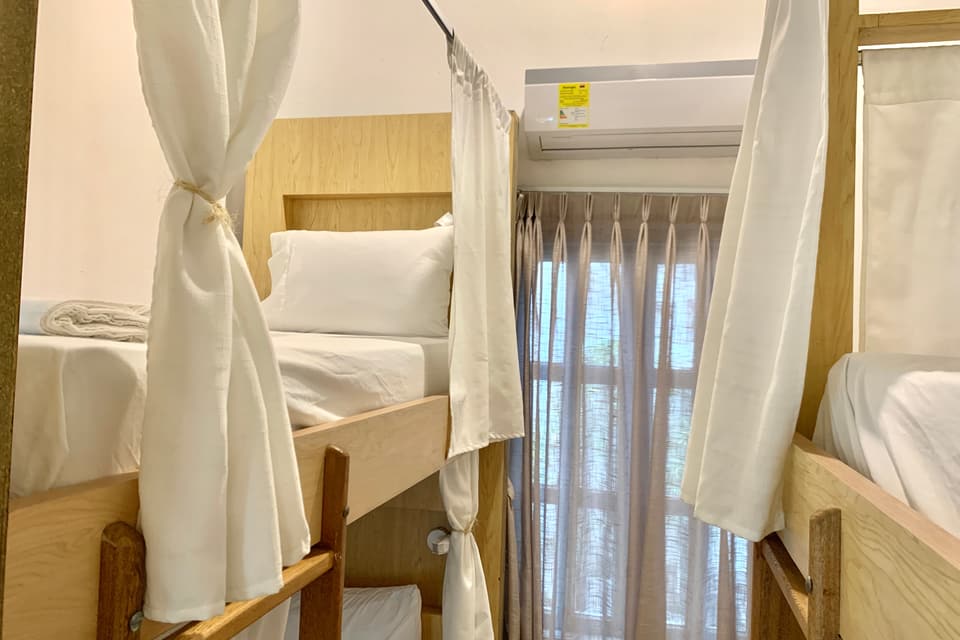 Dormitorio de 6 camas: literas con cortinas blancas, aire acondicionado y ventana con cortinas.