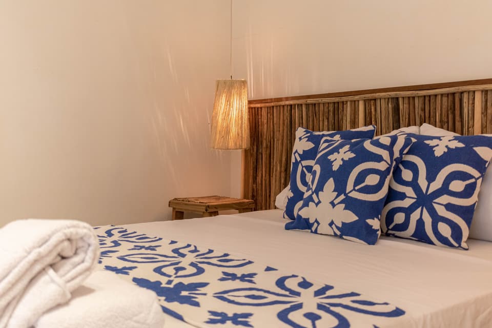 Doble Superior: cama con cabecero de caña, cojines azules con estampado blanco y lámpara colgante de fibra.